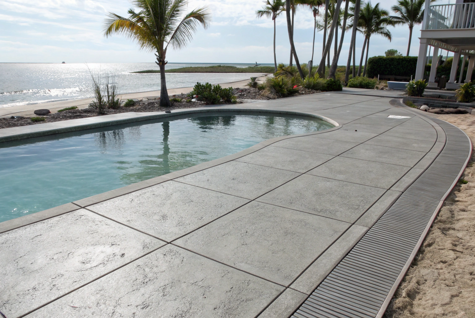 Textured concrete pool surround with a drainage grate beside a beachfront Bundaberg-area home